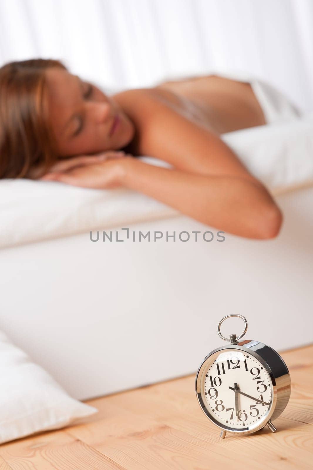 Brown hair woman lying in bed, alarm clock on wooden bed