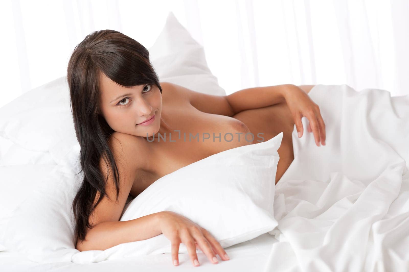 Smiling brown hair woman lying naked in white bed, shallow DOF