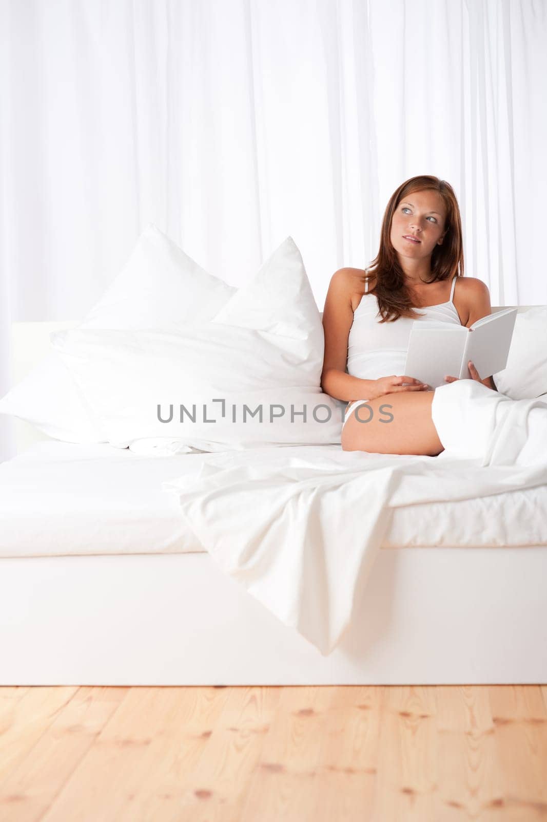 Brown hair woman sitting on white sofa and holding book