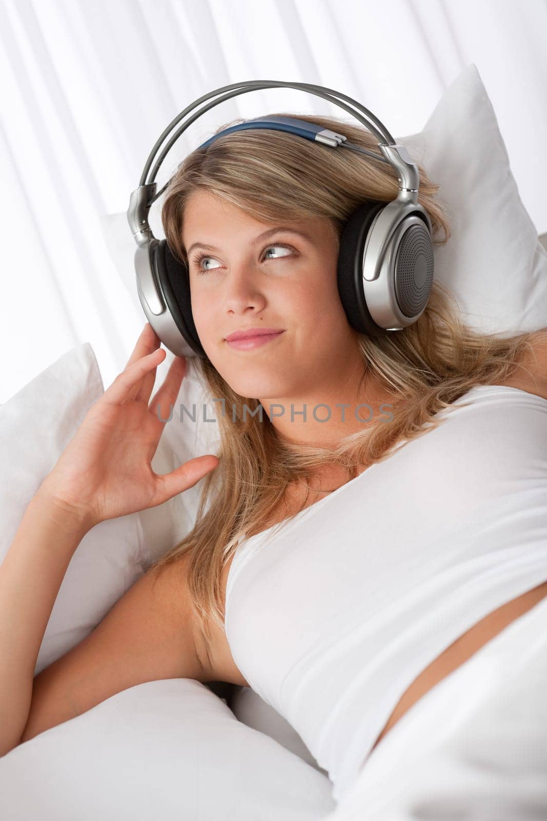 Young smiling woman listening to music with headphones on white sofa