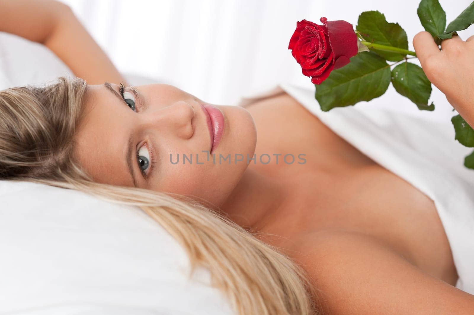 Beautiful woman lying in white bed holding red rose
