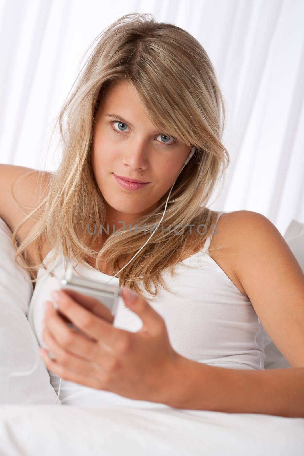 Blond woman holding mp3 player listening to music on white sofa