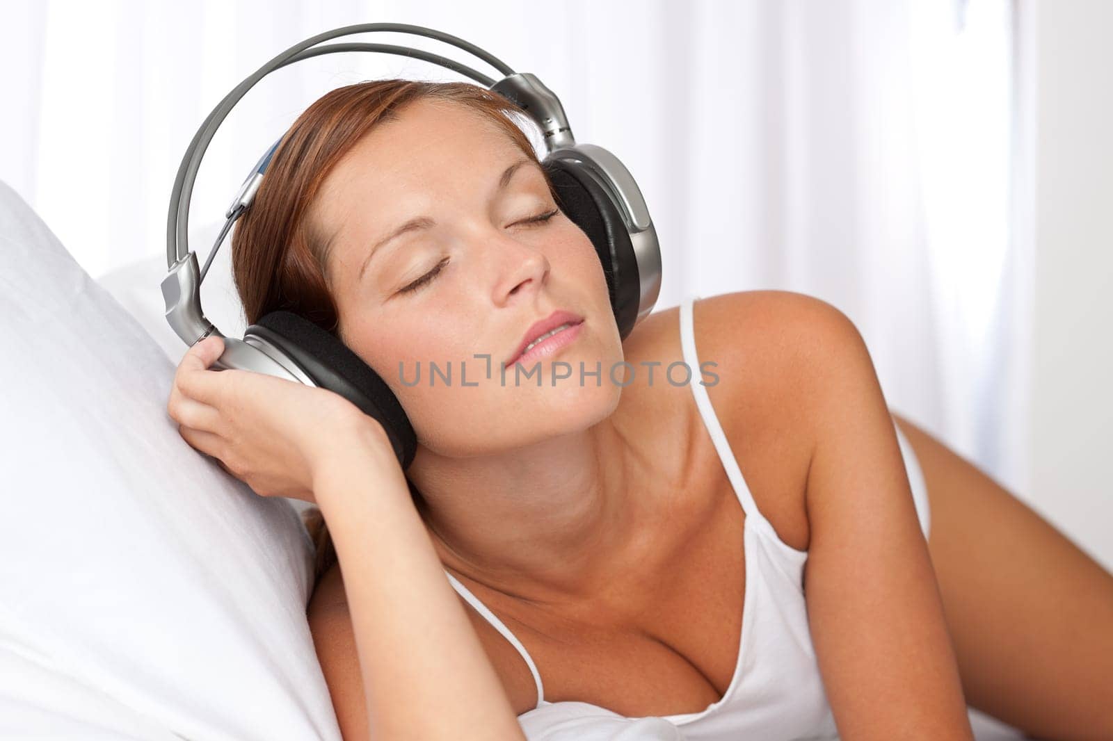 Young woman in white with headphones listening to music in bedroom