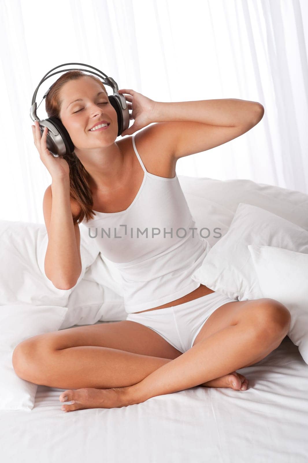 Young woman in white with headphones listening to music in bedroom