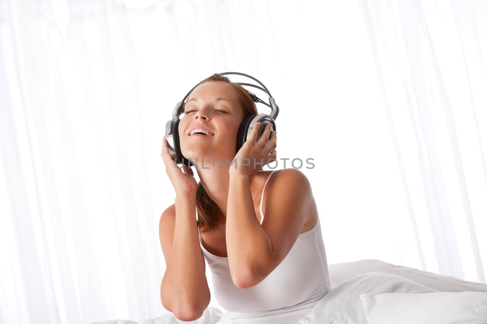 Young woman in white with headphones listening to music in bedroom