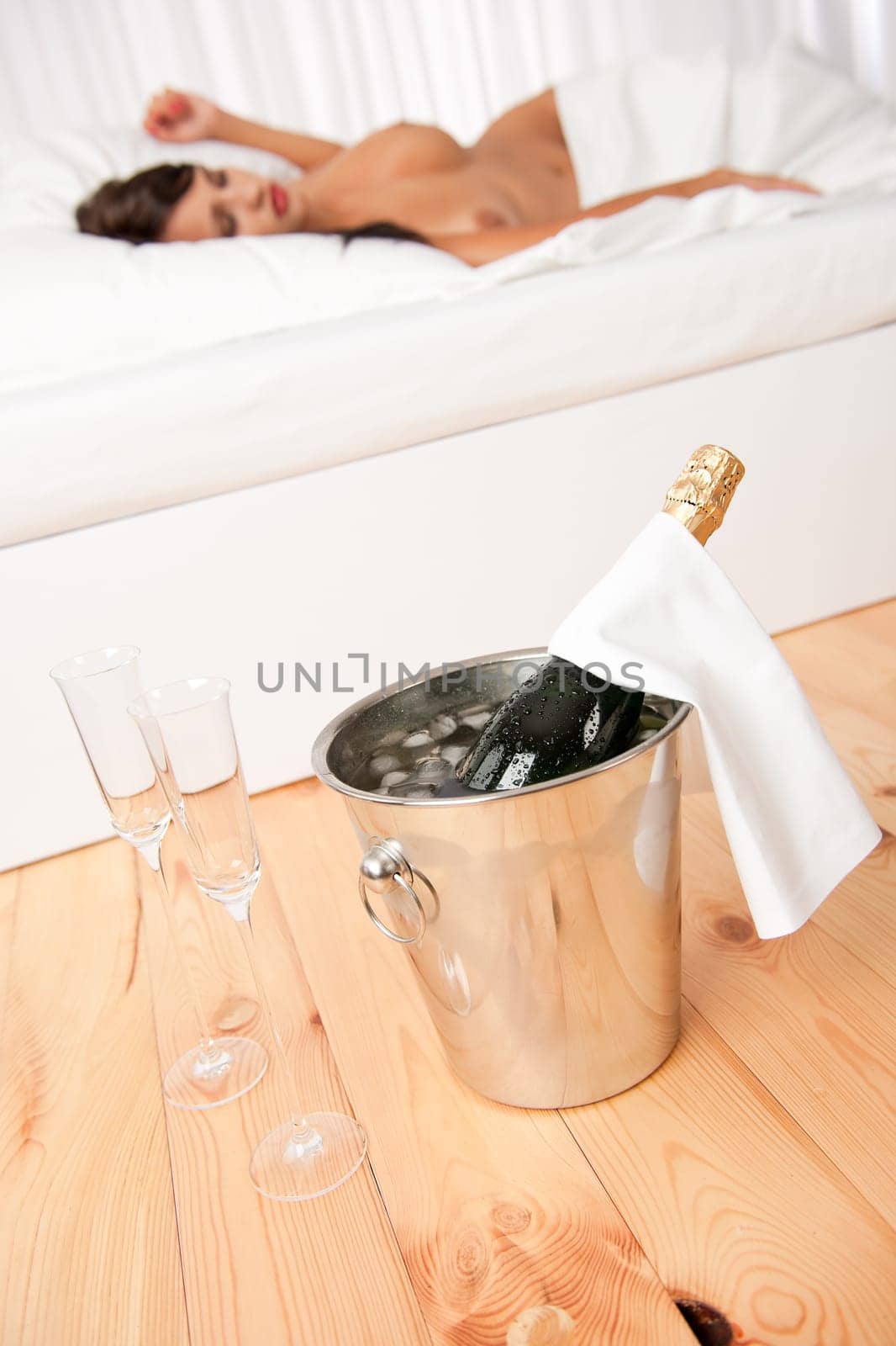 Bottle of champagne in ice bucket, naked woman in background