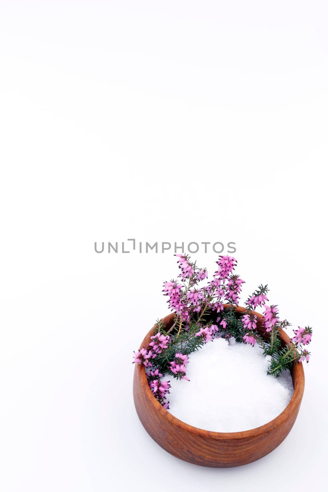 Epsom salts in a teak wood bowl with beautiful heather flowers on a vertical white background.