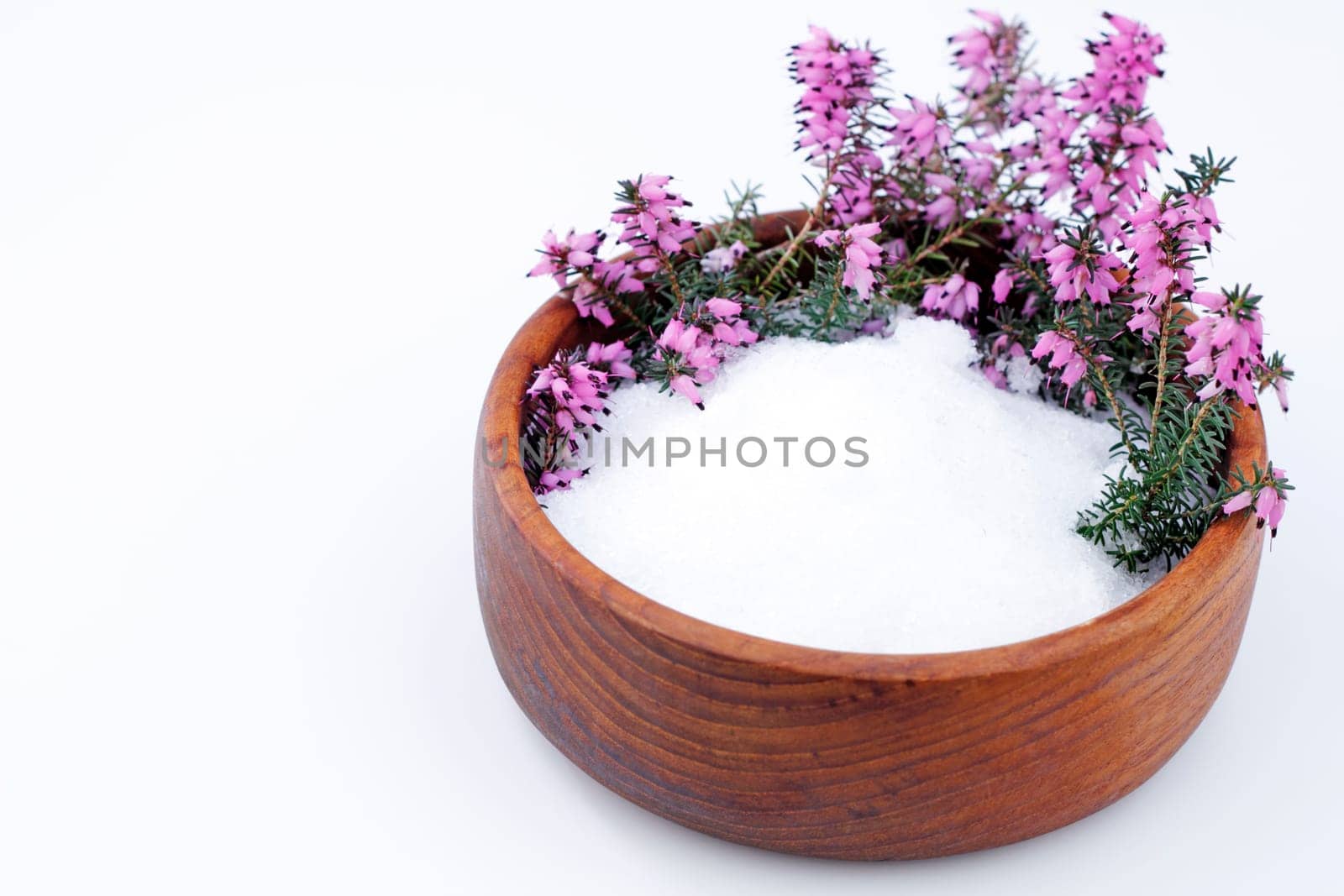 Beautiful purple heather flowers and white Epsom salts wait in a teak wood bowl on a white background.
