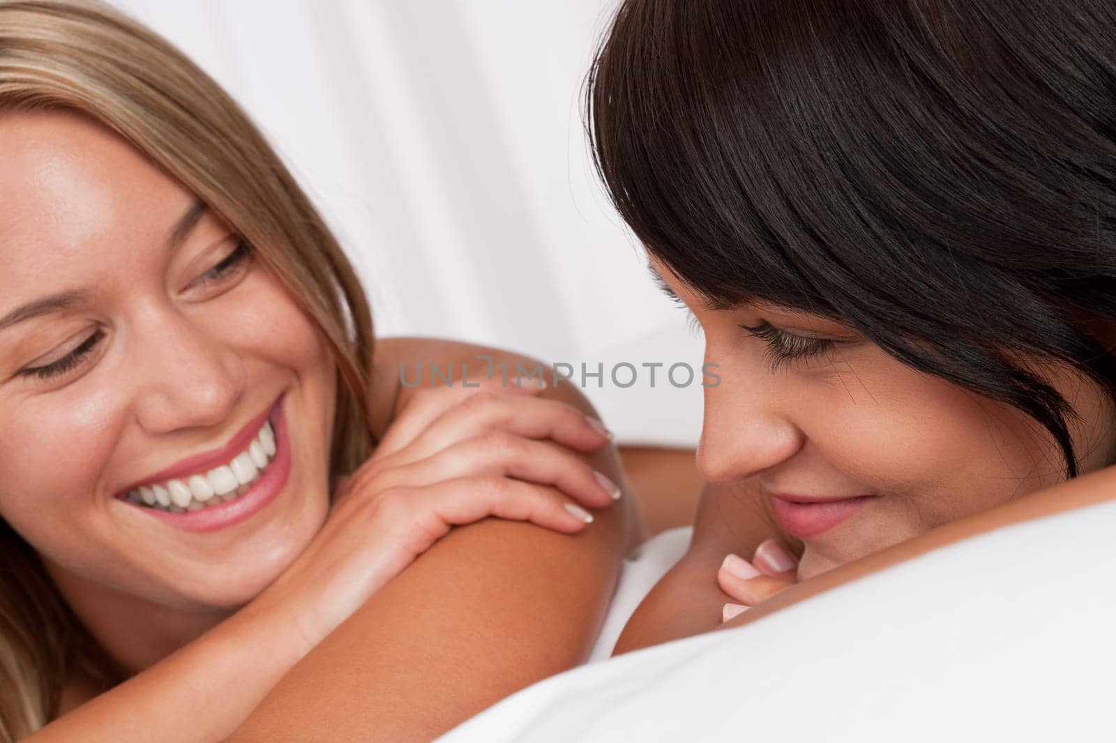 Portrait of two smiling women lying down in white bed having fun