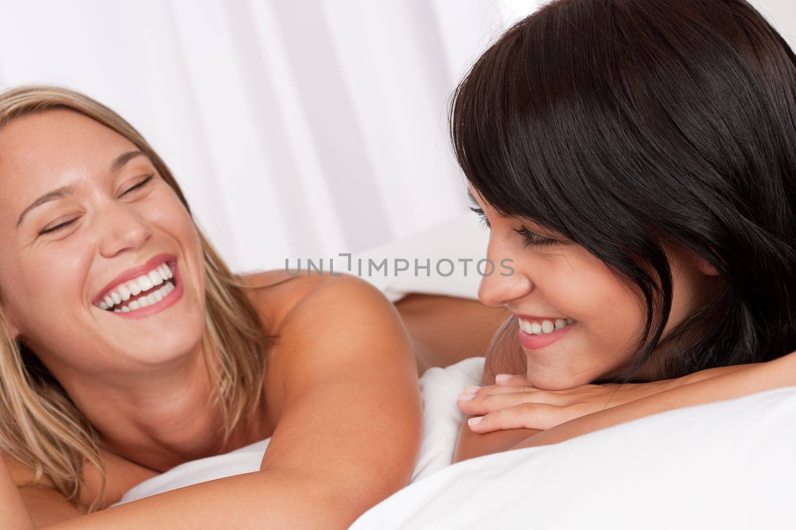 Portrait of two smiling women lying down in white bed having fun