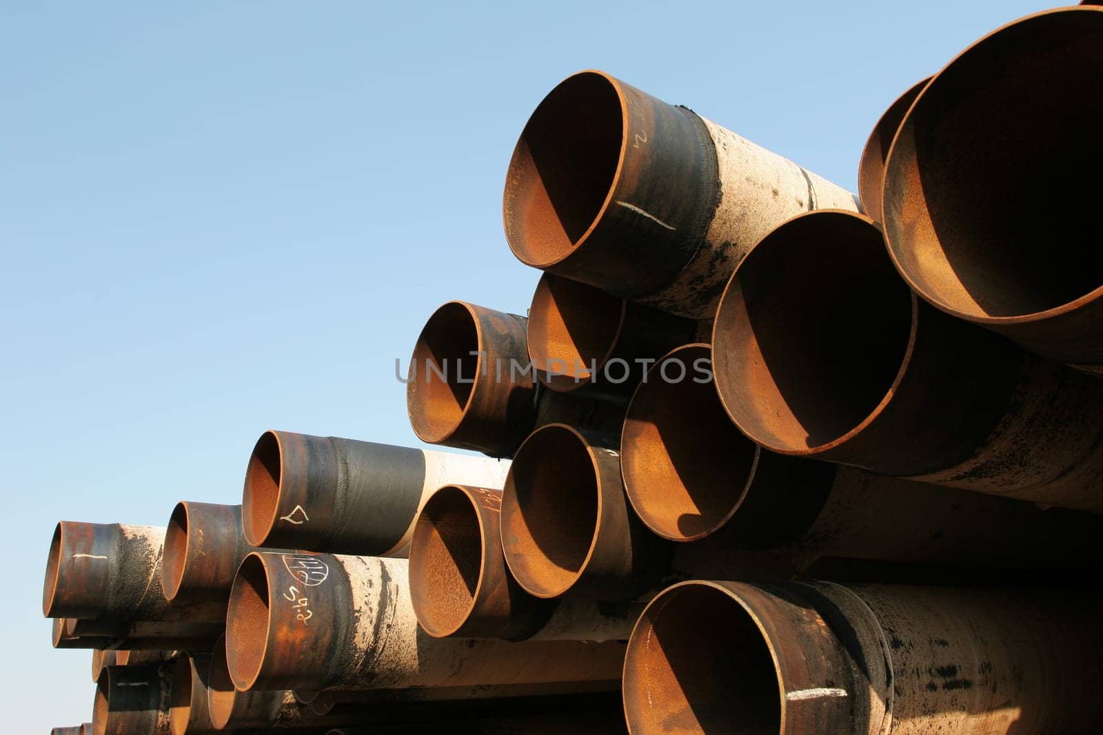 Pile of rusting steel industrial pipes under clear blue sky