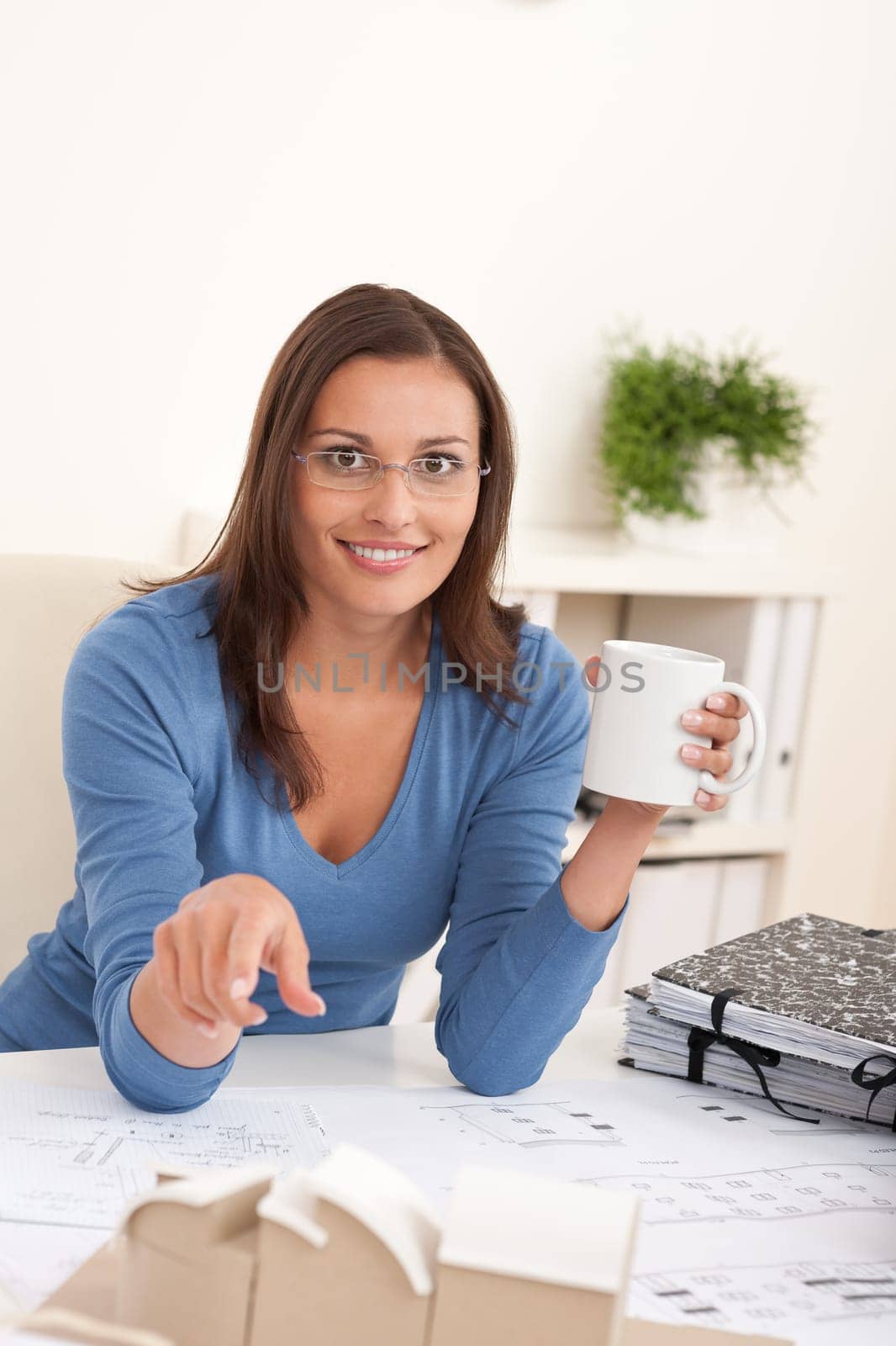 Brown hair female architect sitting at office holding cup of coffee