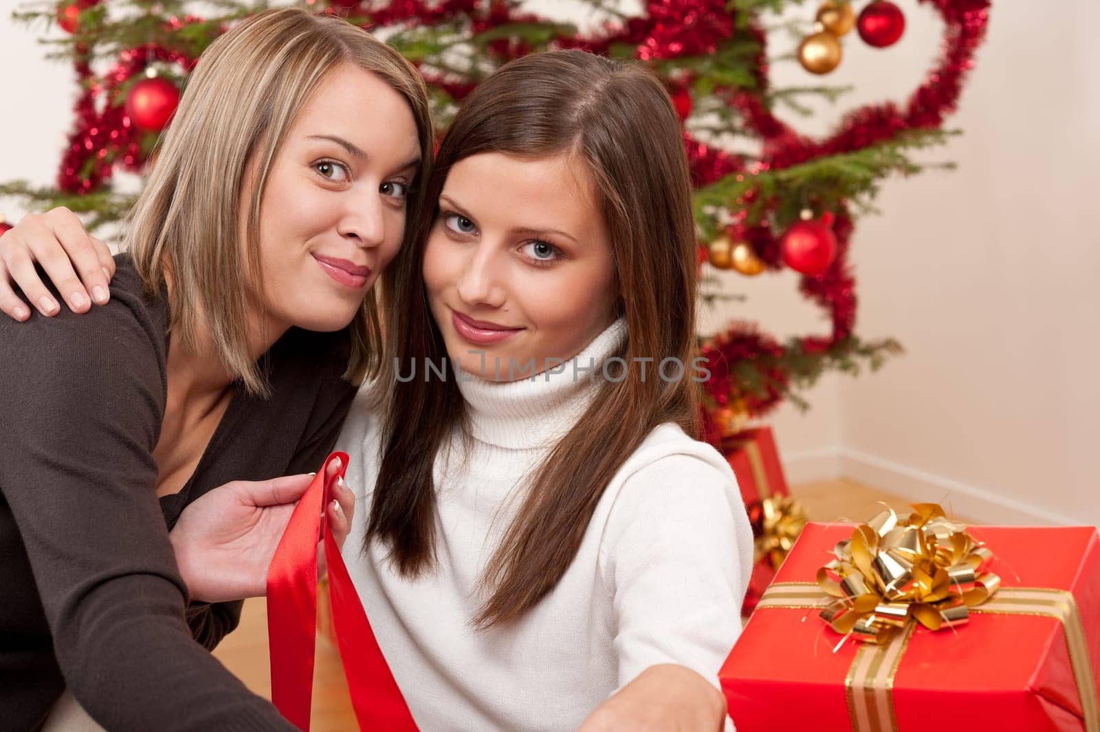 Two young women in front of Christmas tree smiling