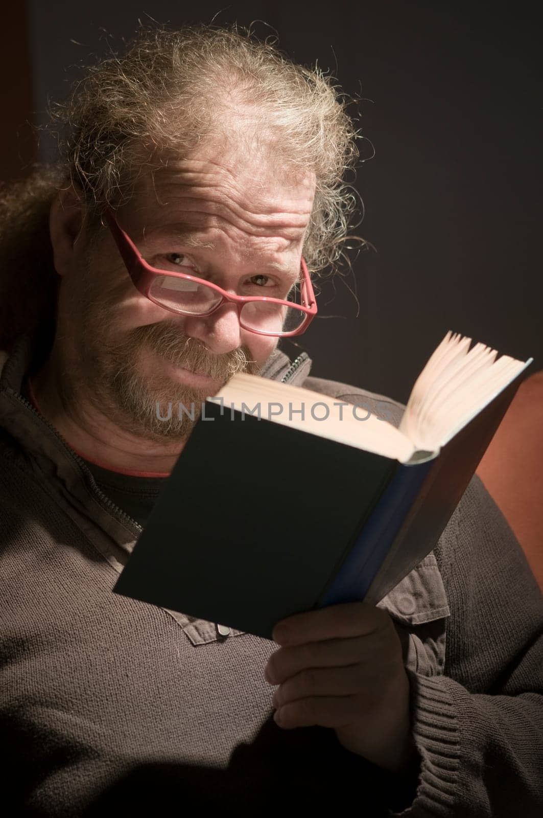 Elderly man with beard,glasses and book reading on sofa at home