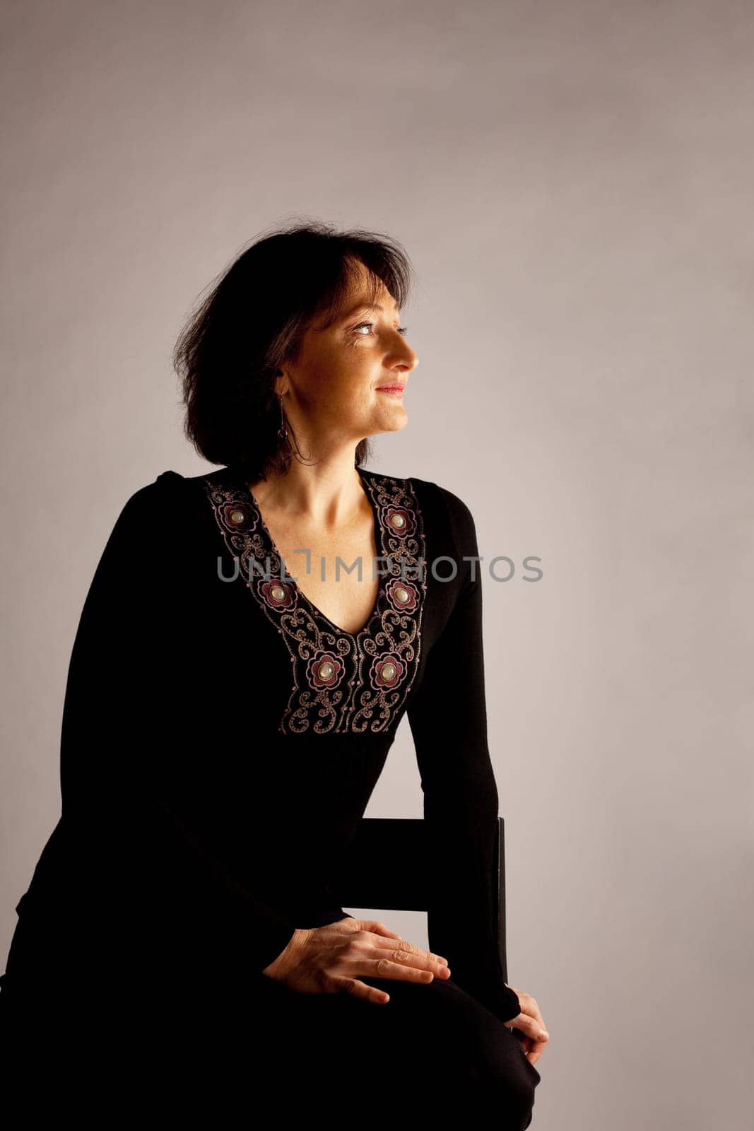 Mature woman in black sit in dark an look light