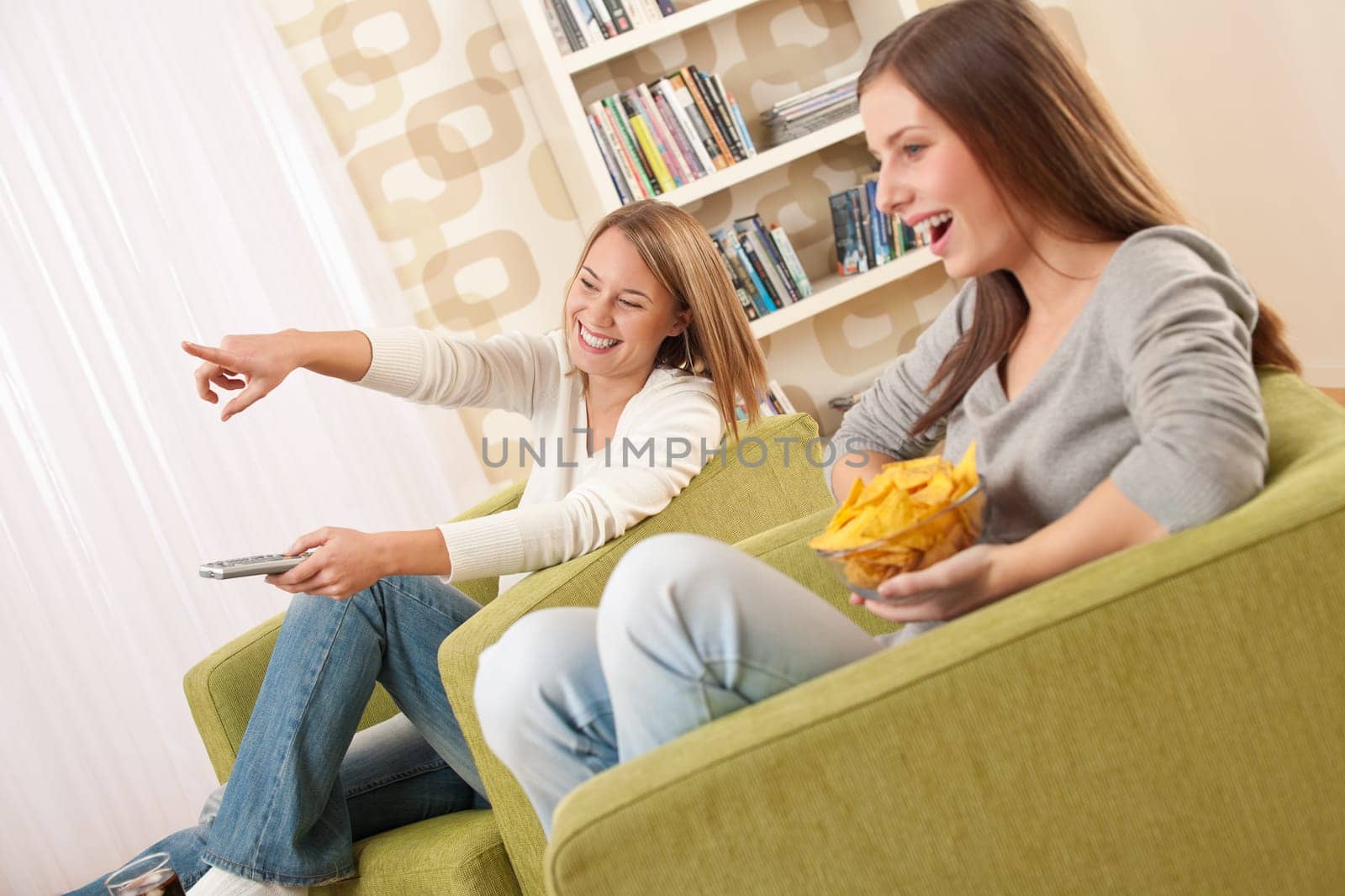 Students - Two female teenager watching television and eating crisps in modern lounge