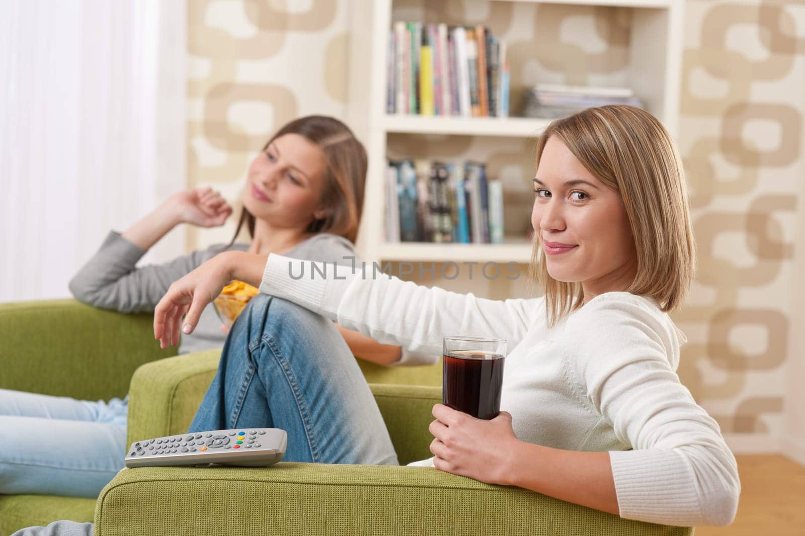 Students - Two smiling female teenager watching television together, eating crisps