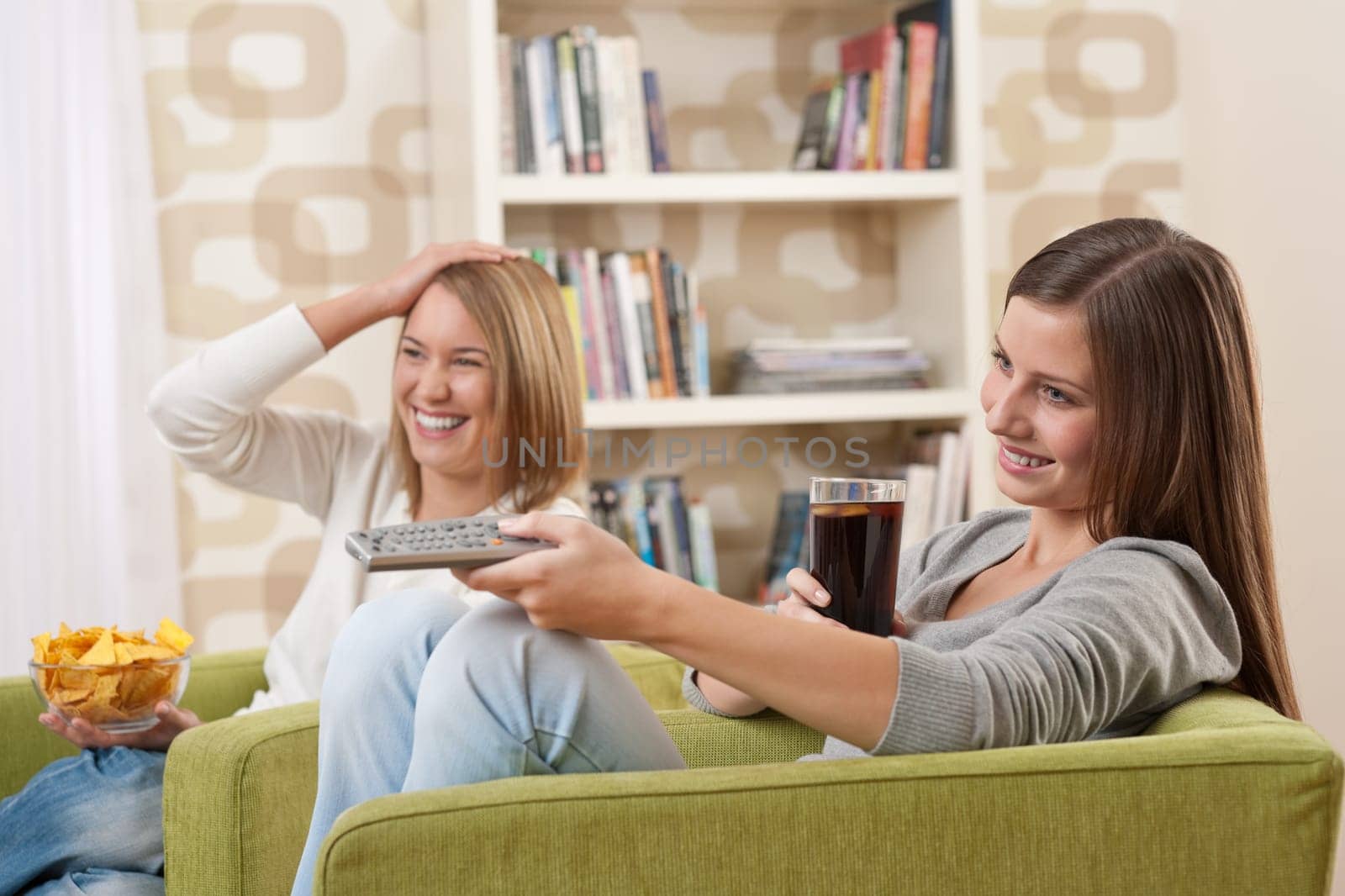 Students - Two female teenager watching television and eating crisps in modern lounge