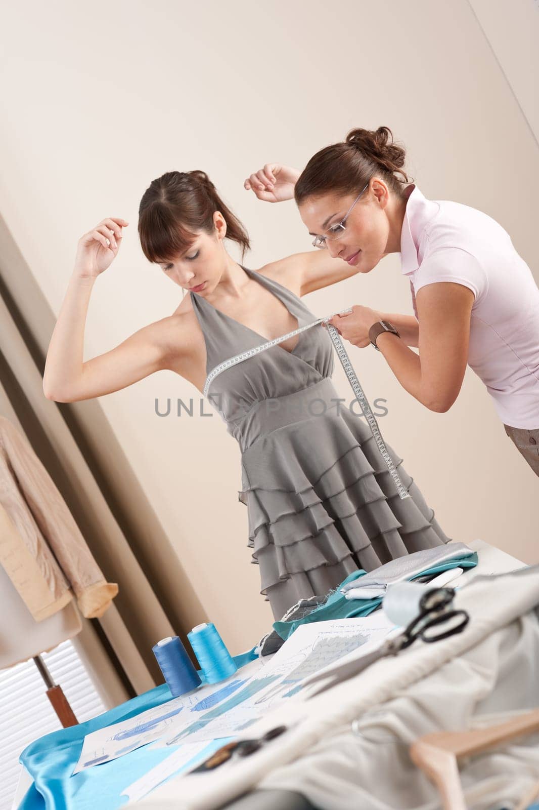 Female fashion designer measuring model for fitting gray dress, taking measurement