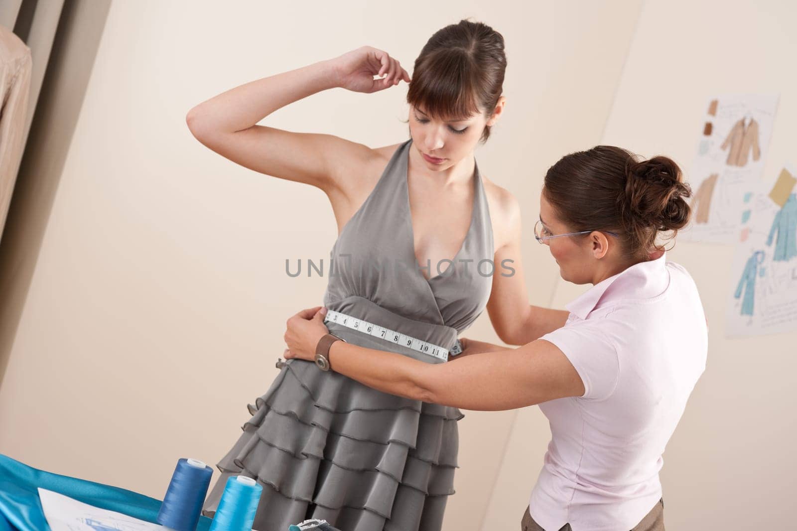 Female fashion designer measuring model for fitting gray dress, taking measurement