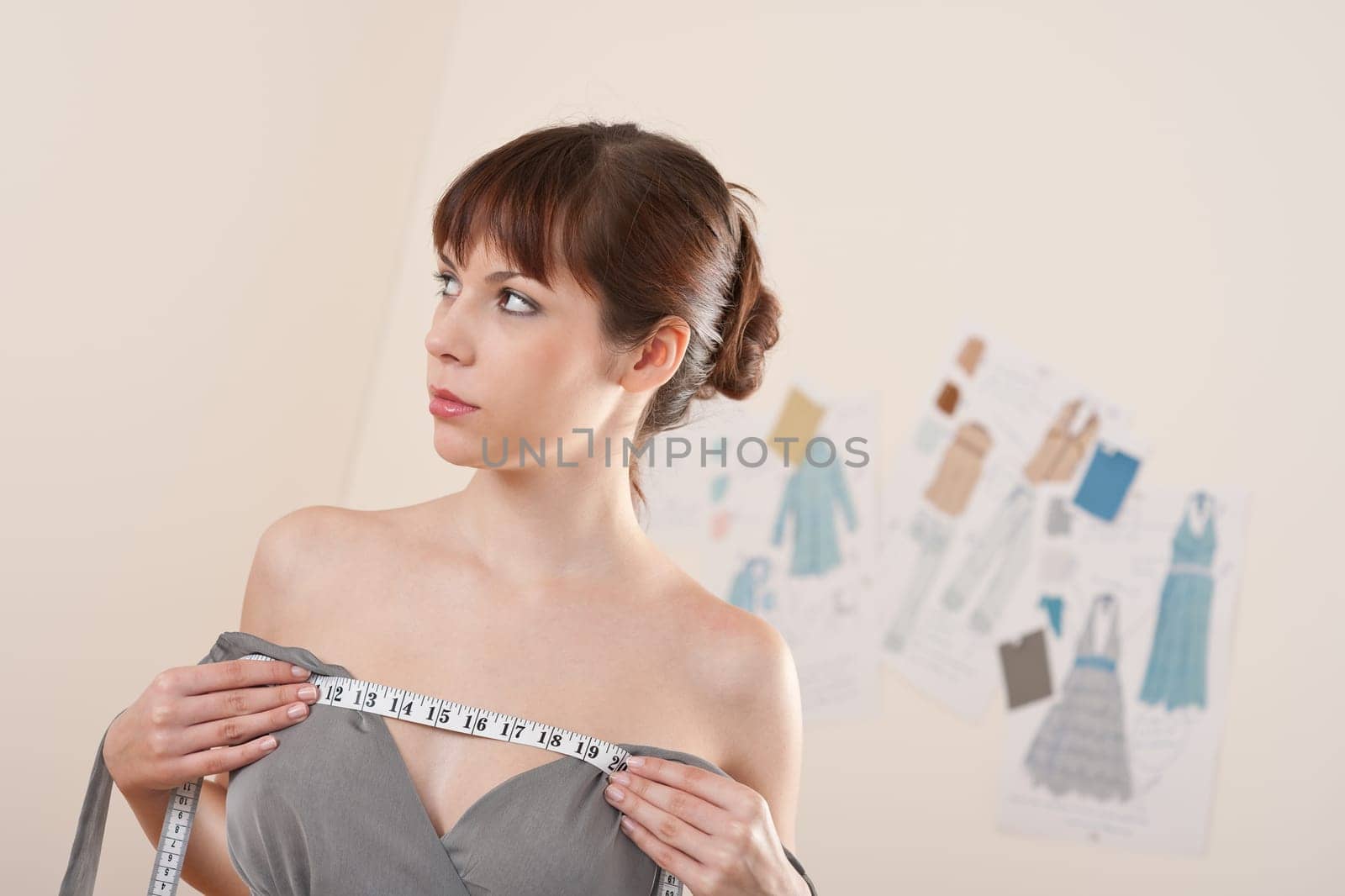 Fashion model trying gray dress in designer studio holding measuring tape