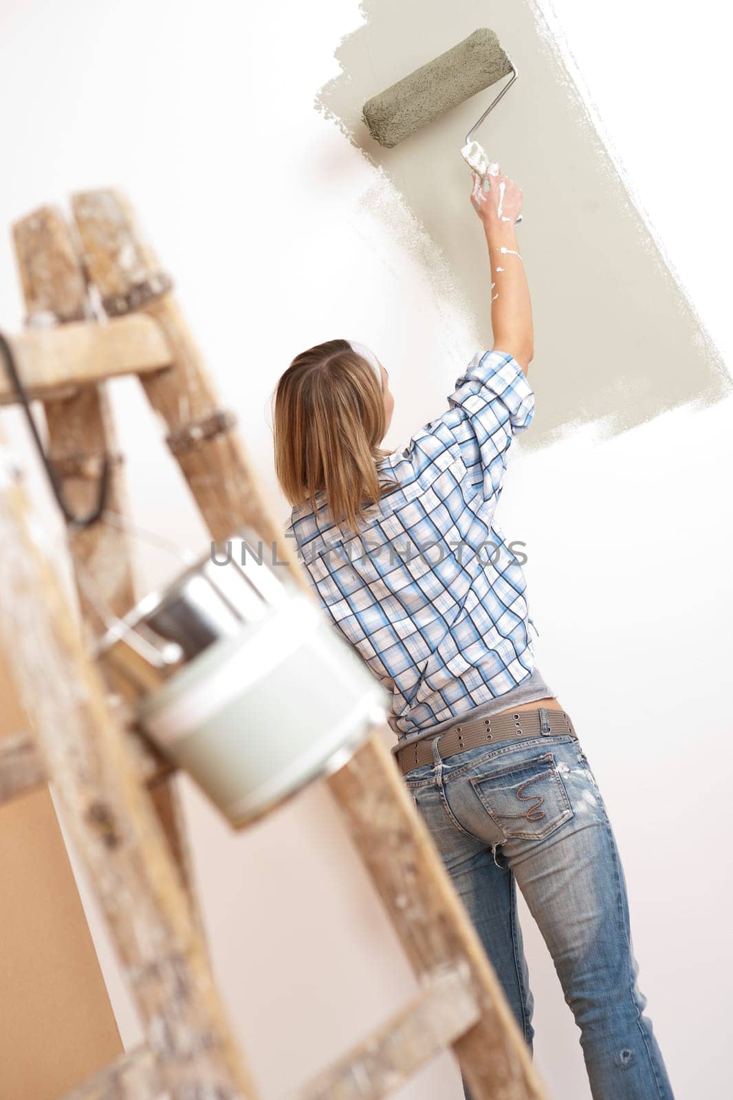 Home improvement: Cheerful woman with paint roller and ladder painting wall