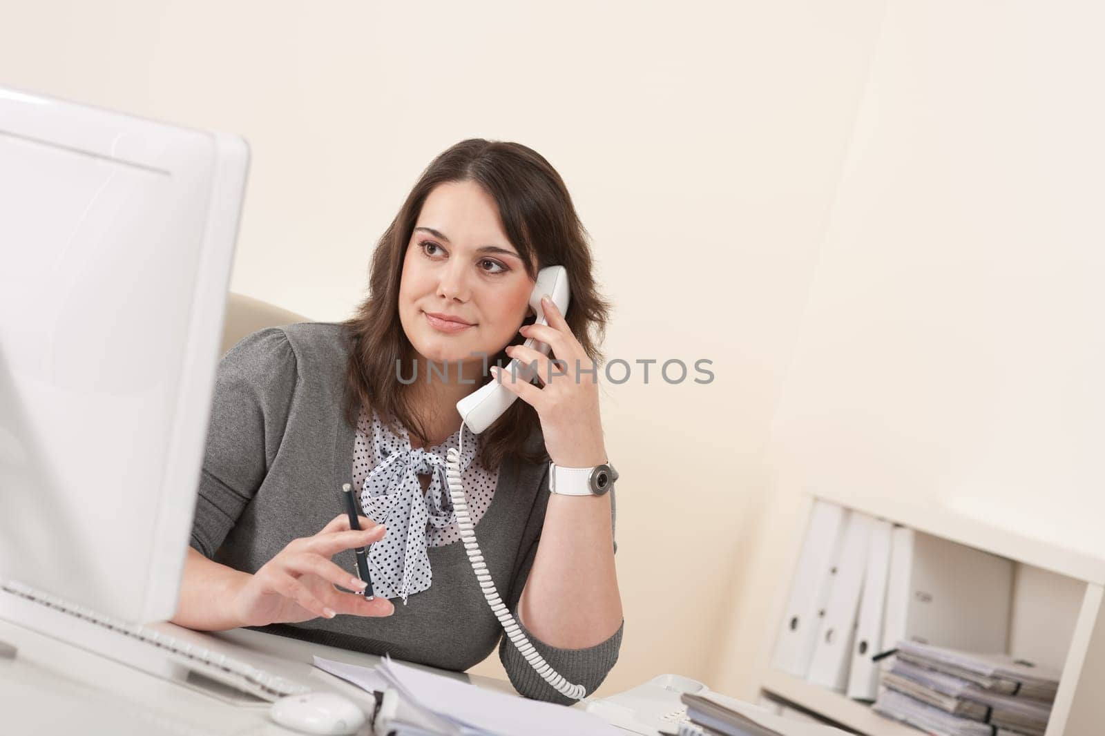 Young woman talking on the phone at office by computer