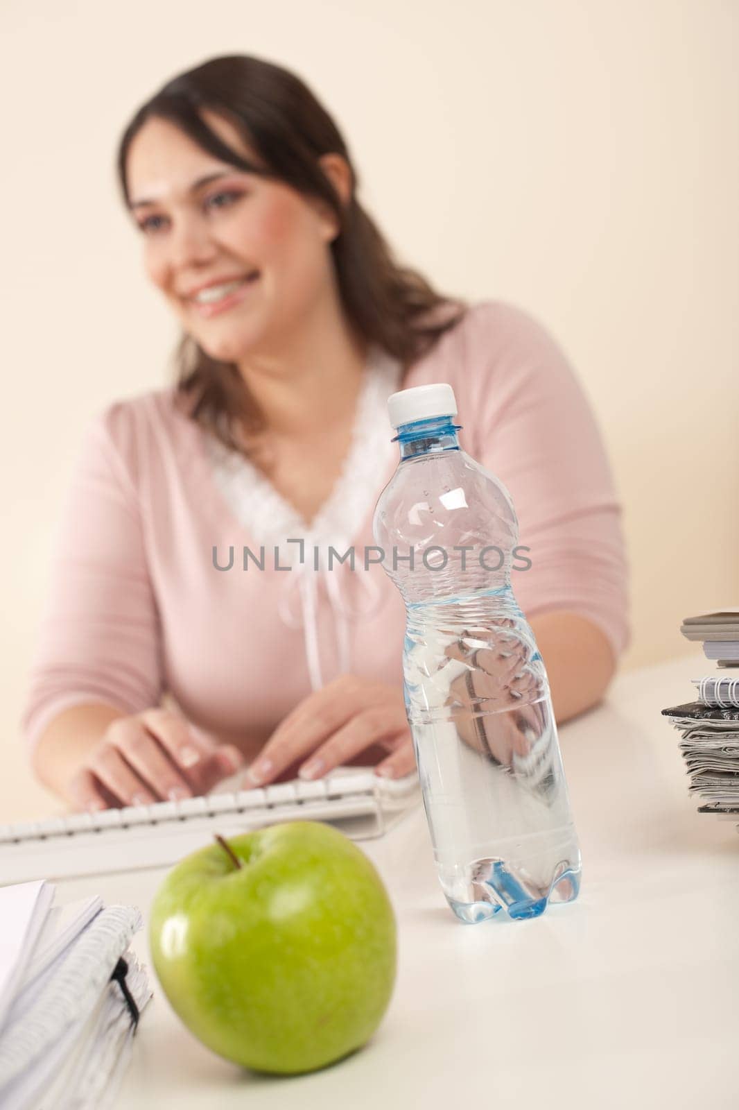 Young businesswoman working at office, focus on apple and bottle of water on table