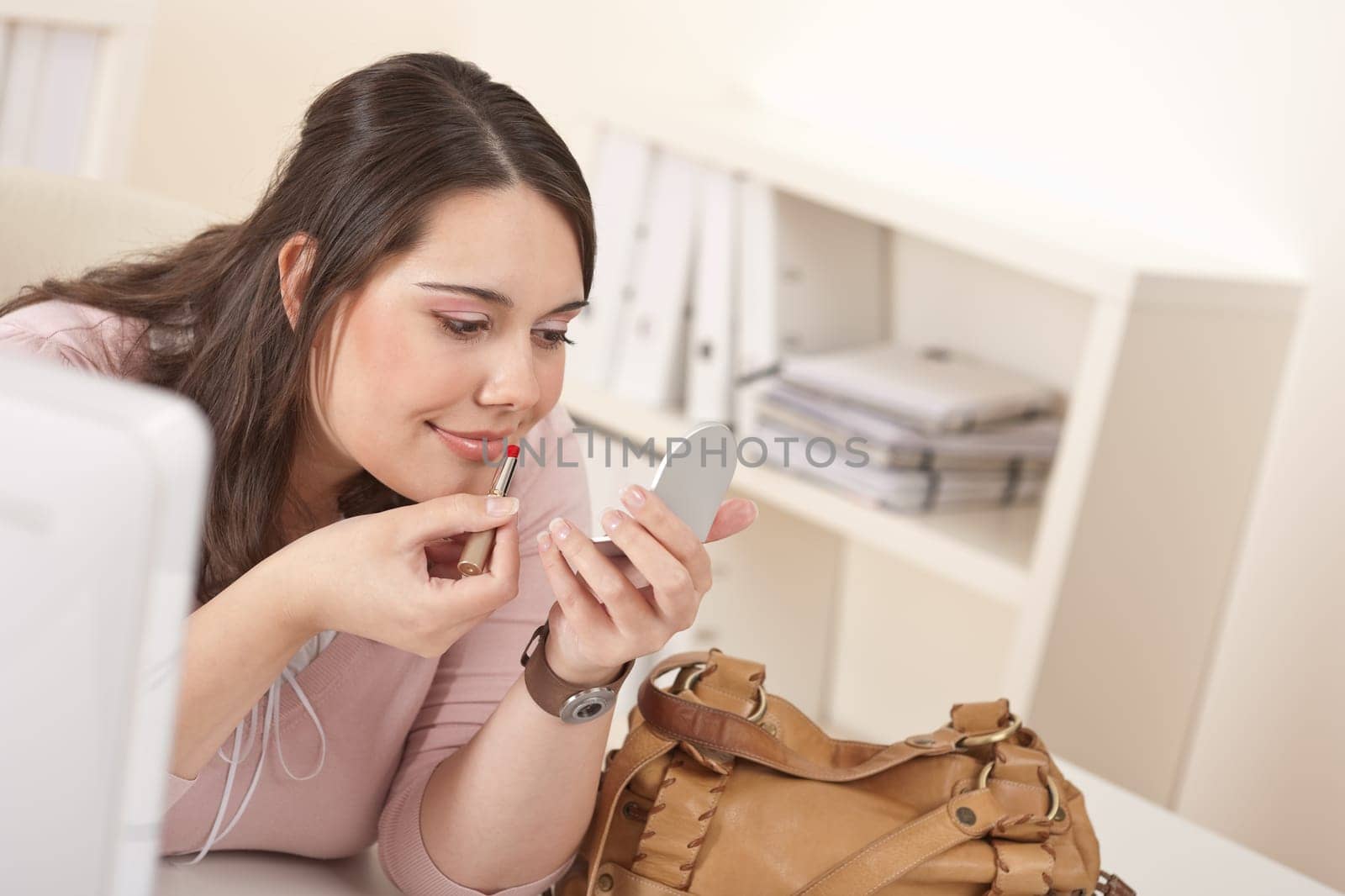 Young executive woman applying lipstick at modern office