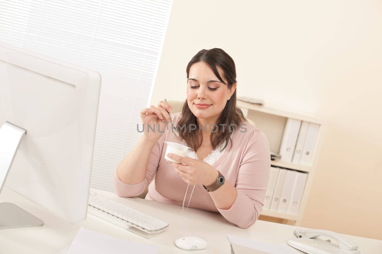 Young businesswoman eating yogurt at office, having break