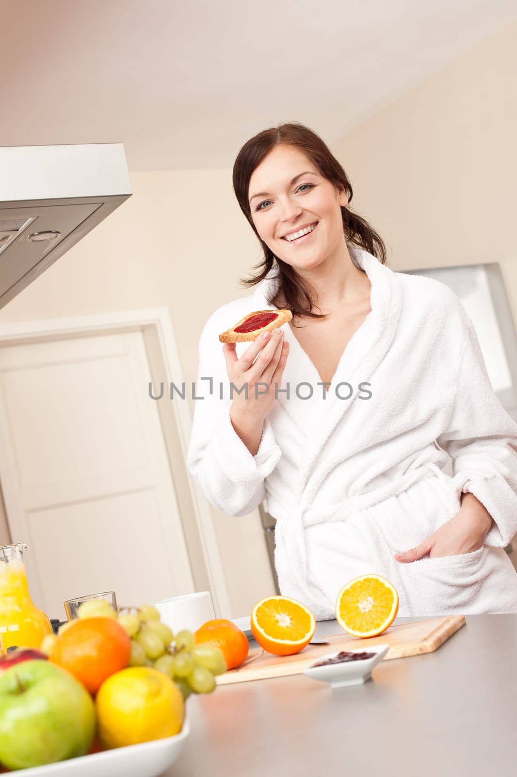 Young woman in bathrobe eating toast for breakfast in kitchen