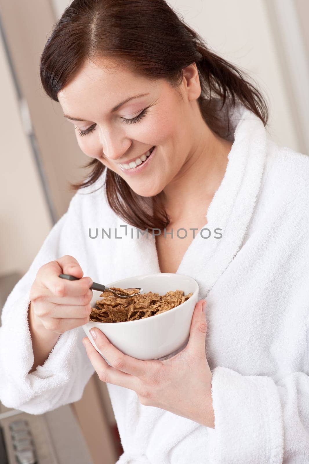 Happy woman in bathrobe holding bowl with cereals for breakfast