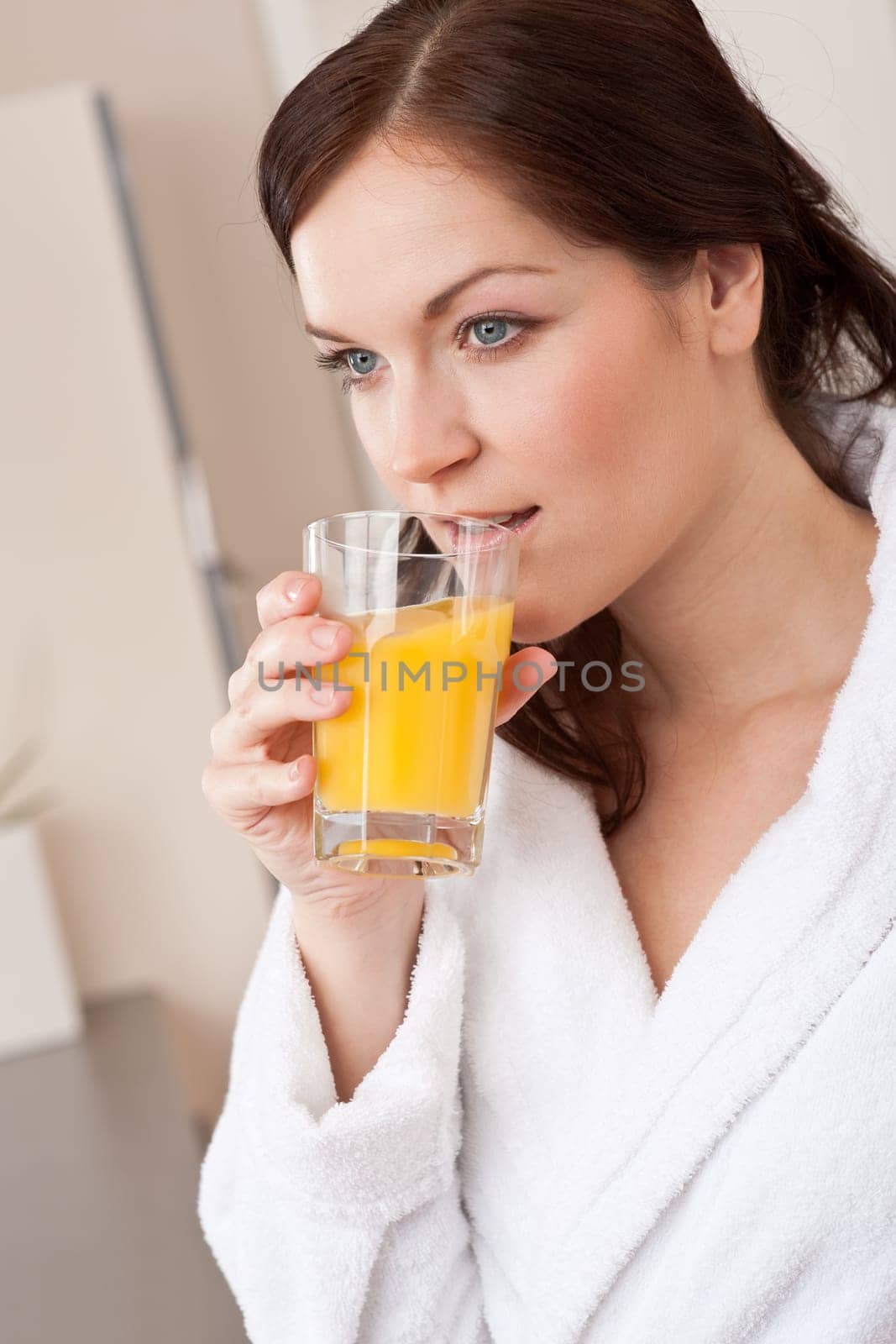 Young woman in bathrobe drink orange juice for breakfast in kitchen
