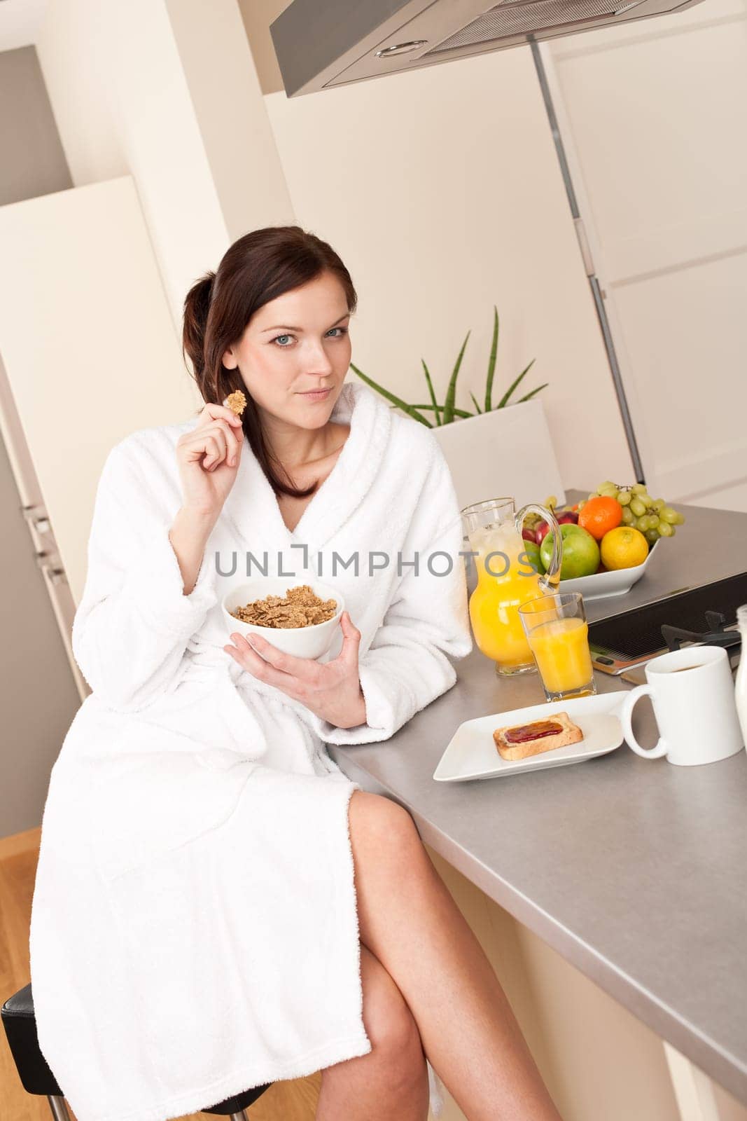 Happy woman in bathrobe eating healthy cereals for breakfast in kitchen