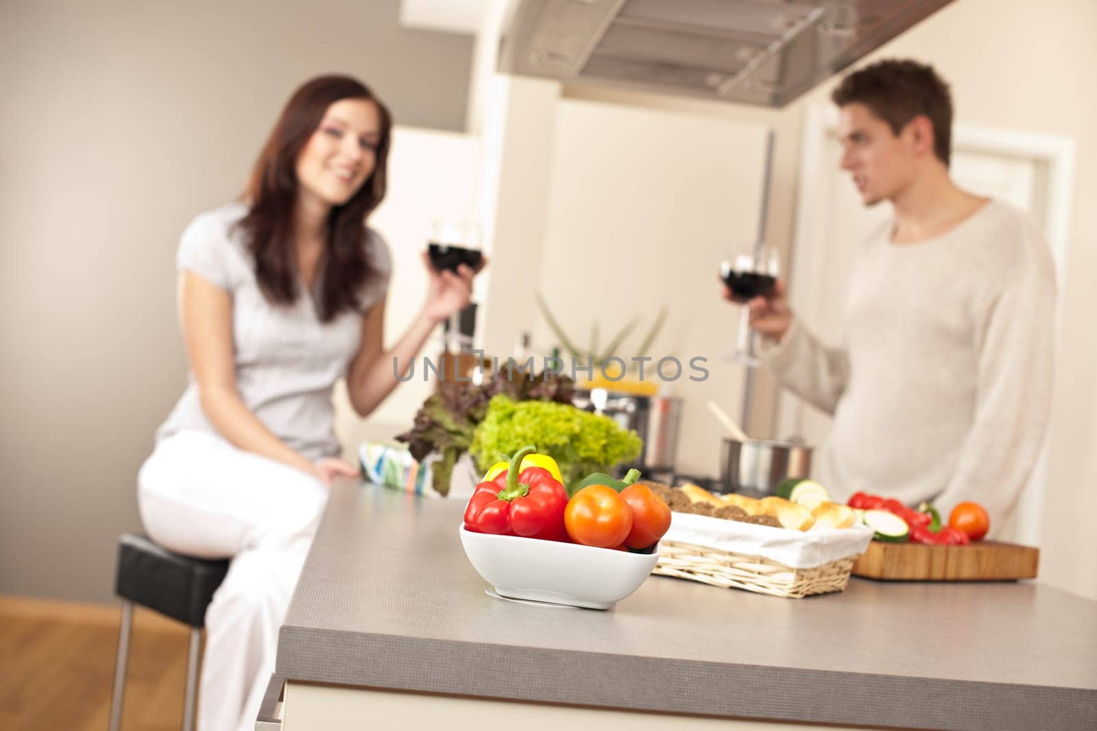 Young couple drinking red wine in kitchen, focus on bowl with vegetable