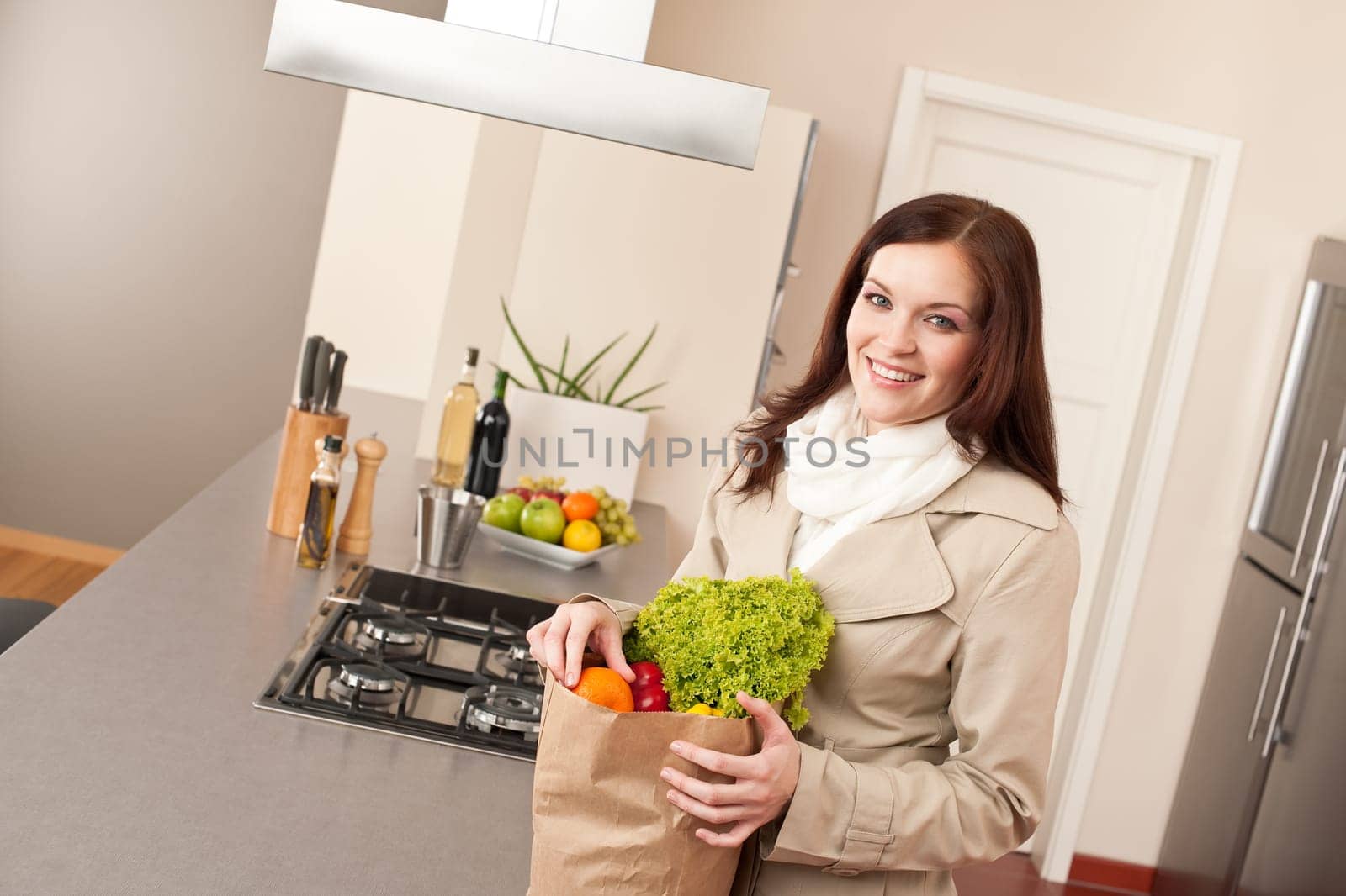 Smiling woman holding shopping bag with grocery in kitchen