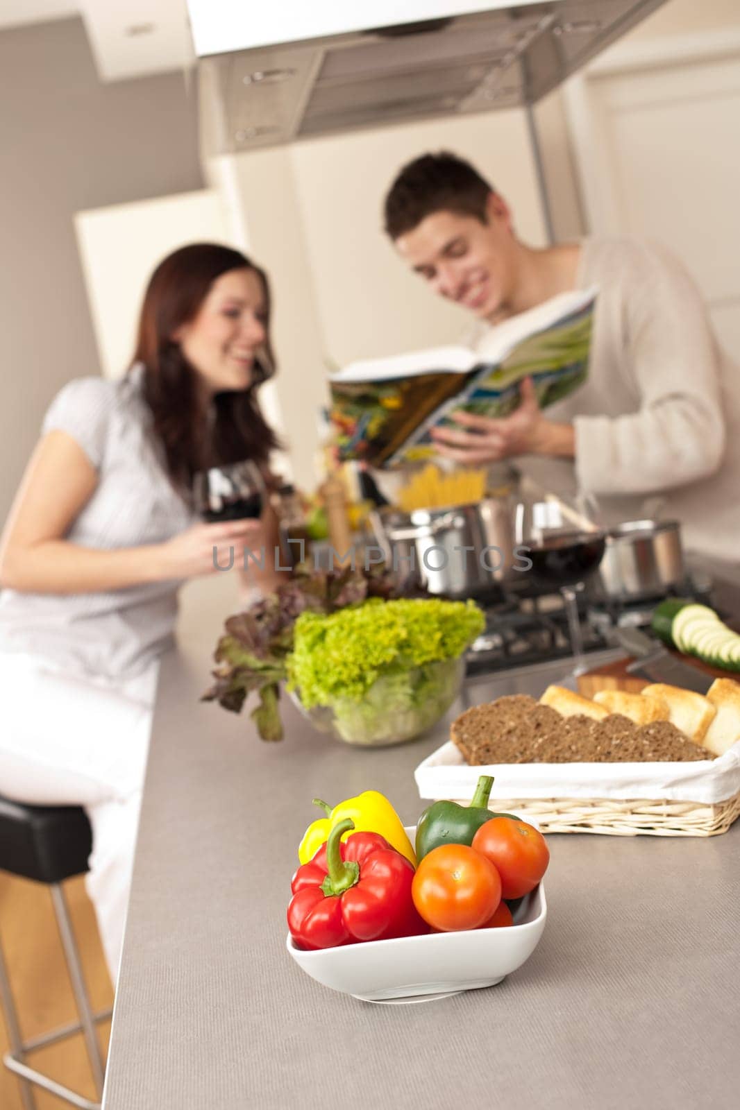 Young couple in kitchen choosing recipe from cookbook drinking red wine