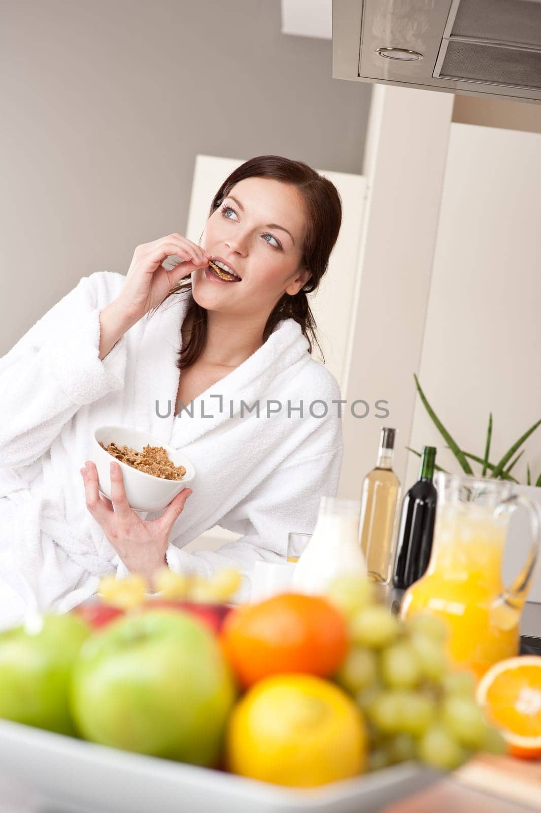 Happy woman in bathrobe eat cereals for breakfast in kitchen