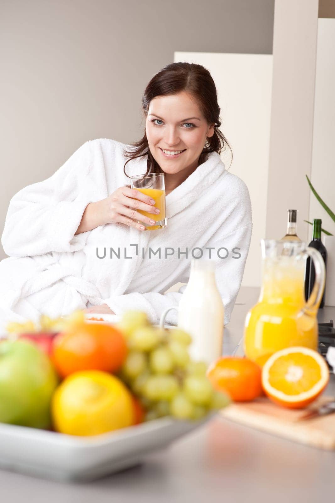 Young woman in bathrobe drink orange juice for breakfast in kitchen