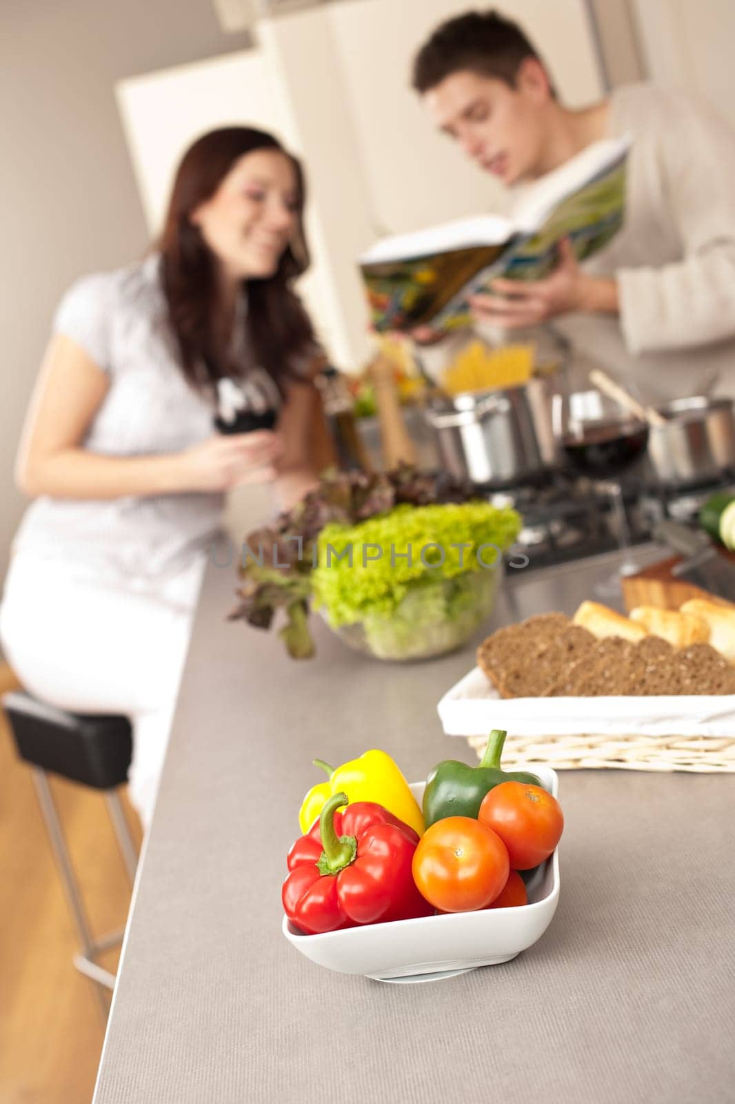 Young couple in kitchen choosing recipe from cookbook drinking red wine