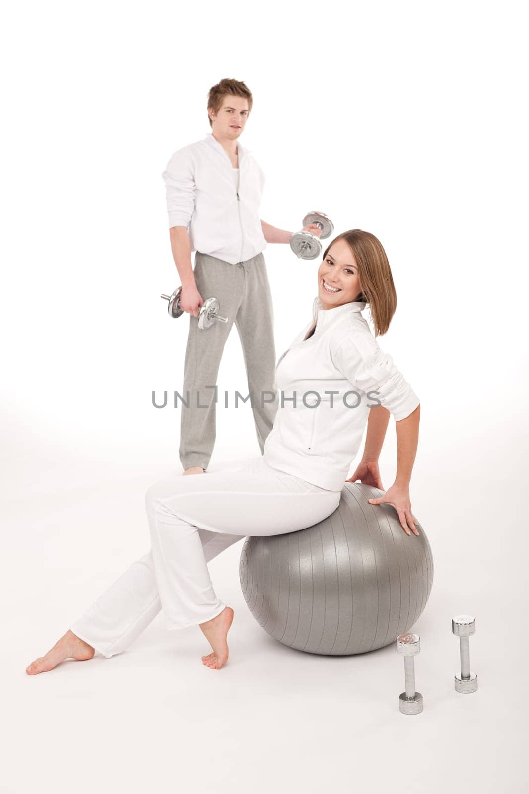 Young healthy couple training with weights and fitness ball on white