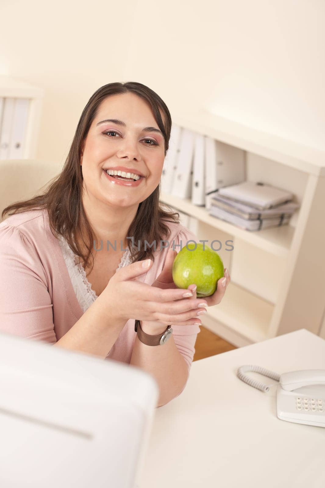 Young happy businesswoman holding apple at office having snack