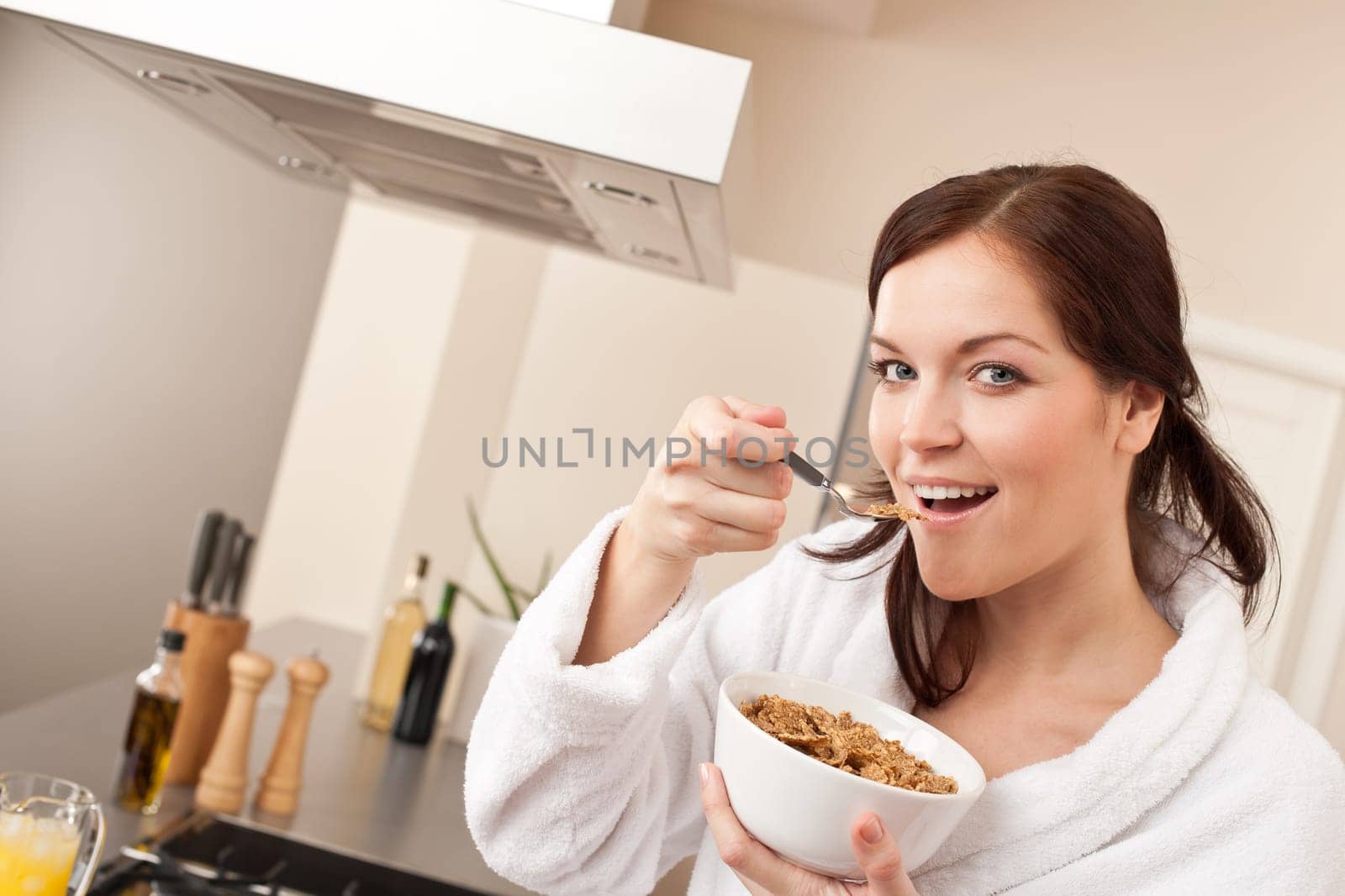 Happy woman in bathrobe eating healthy cereals for breakfast in kitchen