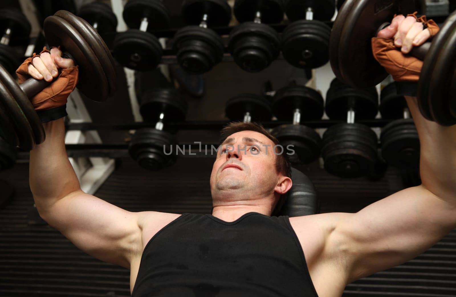 training dumbbells in gym. Male lifting weights for upper body strength building pecks, shoulders and biceps