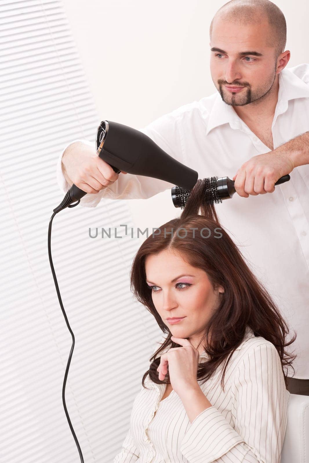 Professional male hairdresser with hair dryer at salon with female customer