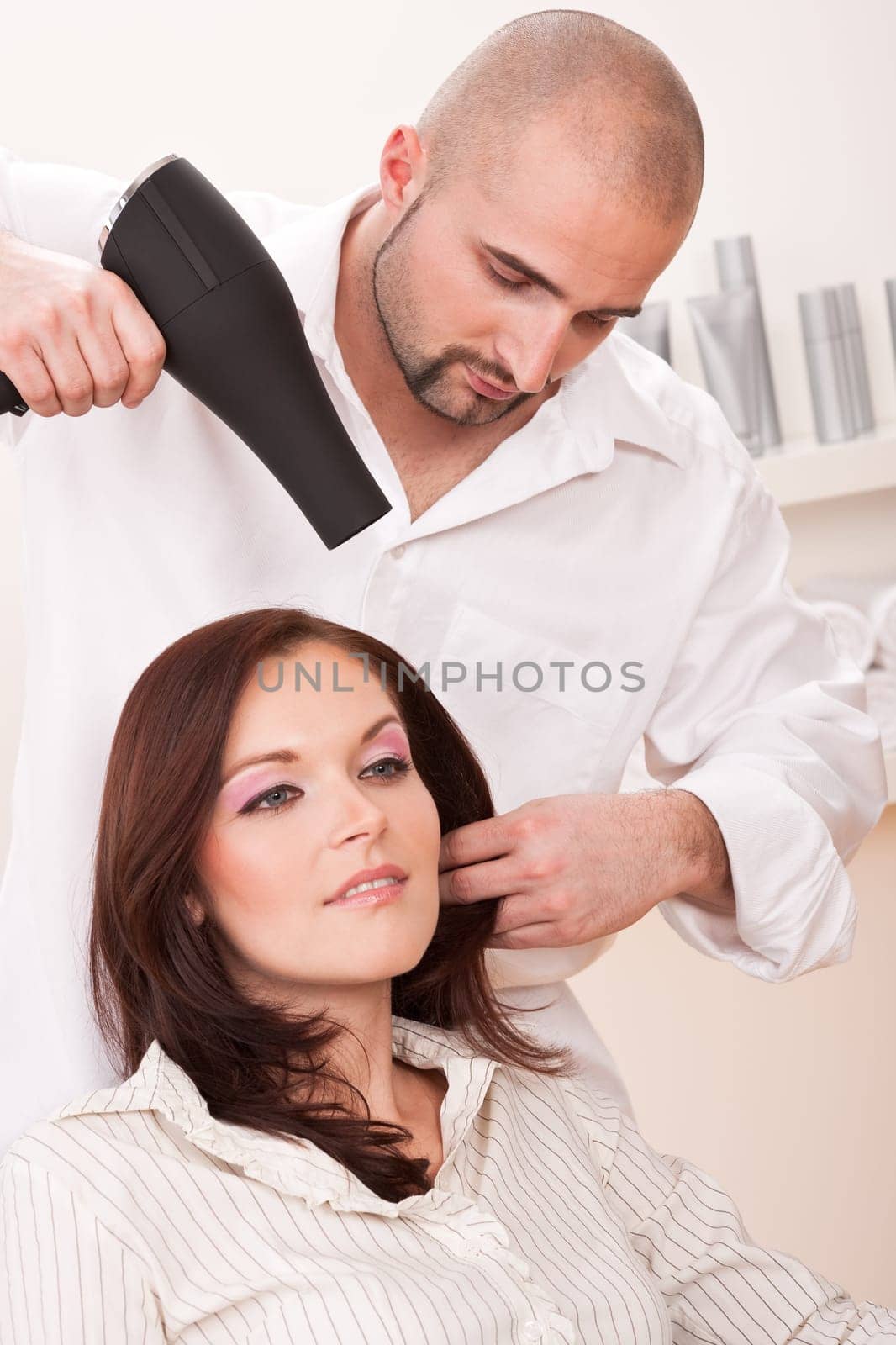 Professional male hairdresser with hair dryer at salon with female customer