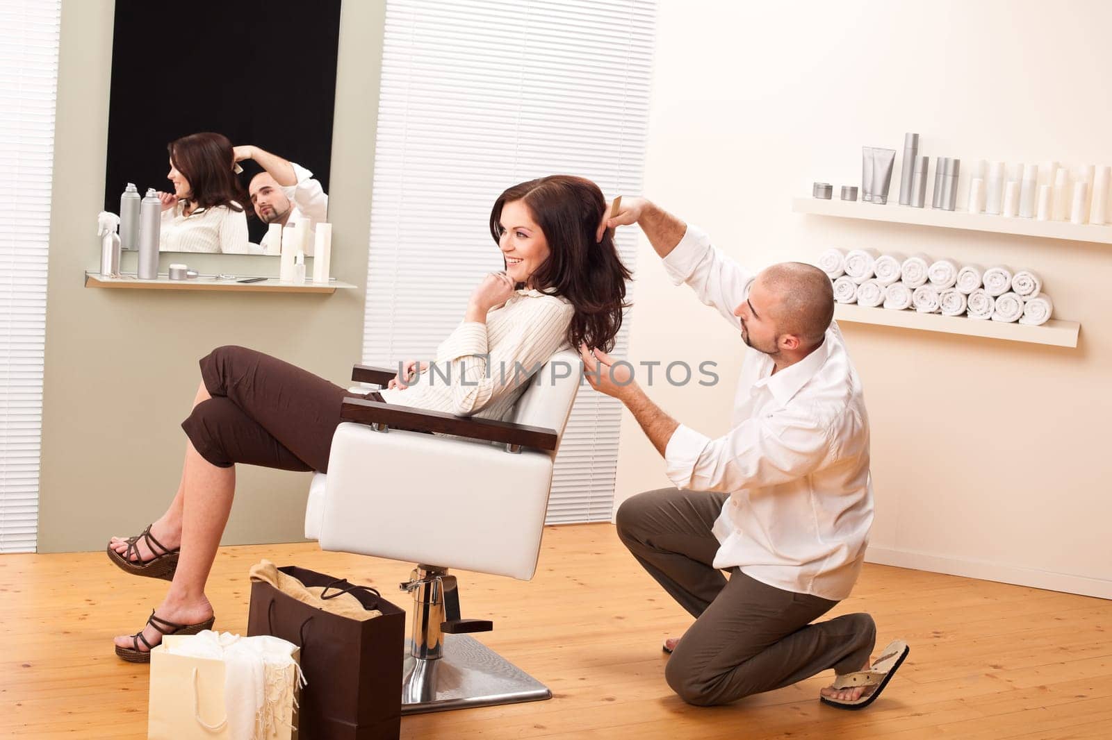 Professional male hairdresser comb female customer at salon, shopping bags on floor