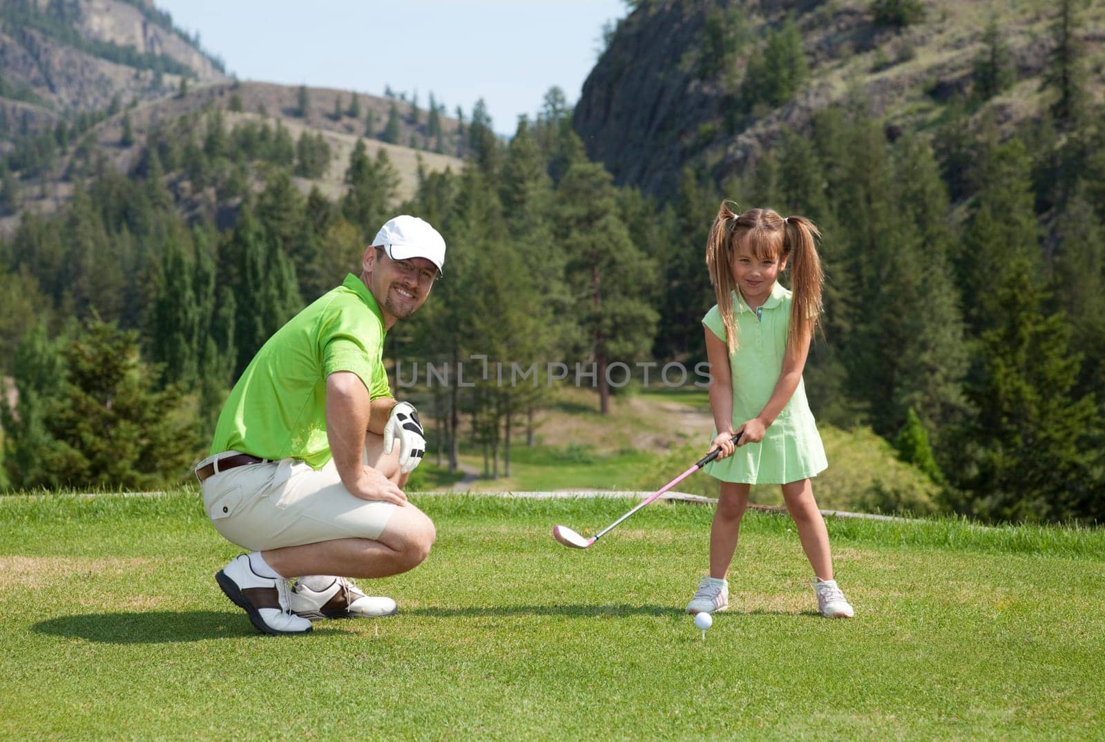Outdoor photo of father and youngster daughter on golf course.