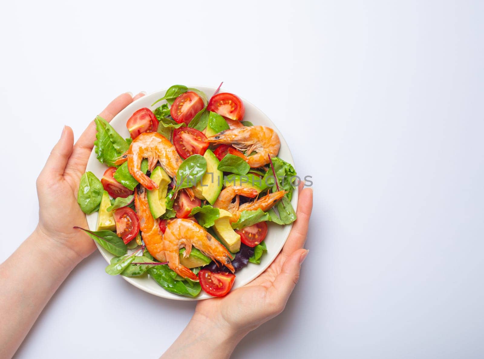 Female hands holding healthy salad with grilled shrimps, avocado, cherry tomatoes and green leaves on white plate isolated on white background top view. Clean eating, nutrition and dieting concept. by its_al_dente