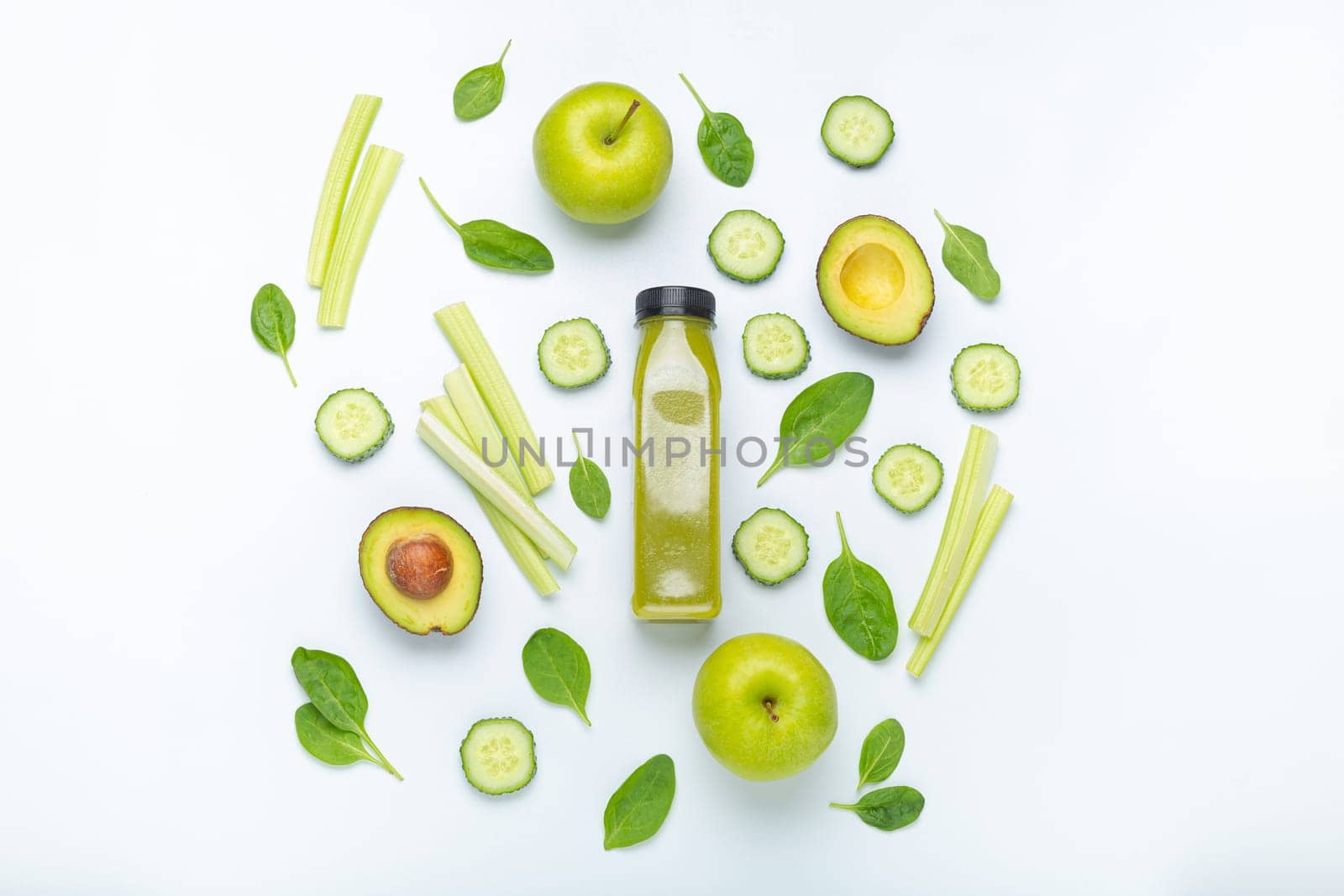 Bottle of green smoothie surrounded by green fruit and vegetables: apples, avocado, spinach, celery sticks, cucumber on white simple background top view. Diet, healthy nutrition, detox by its_al_dente